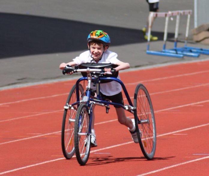 A boy wearing a helmet is running using a metal frame with three wheels